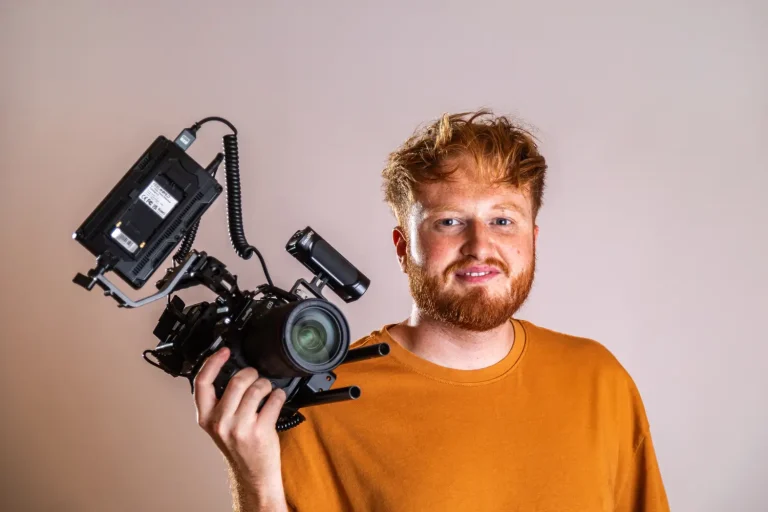 Dan Dennis looking towards the camera holding a camera.